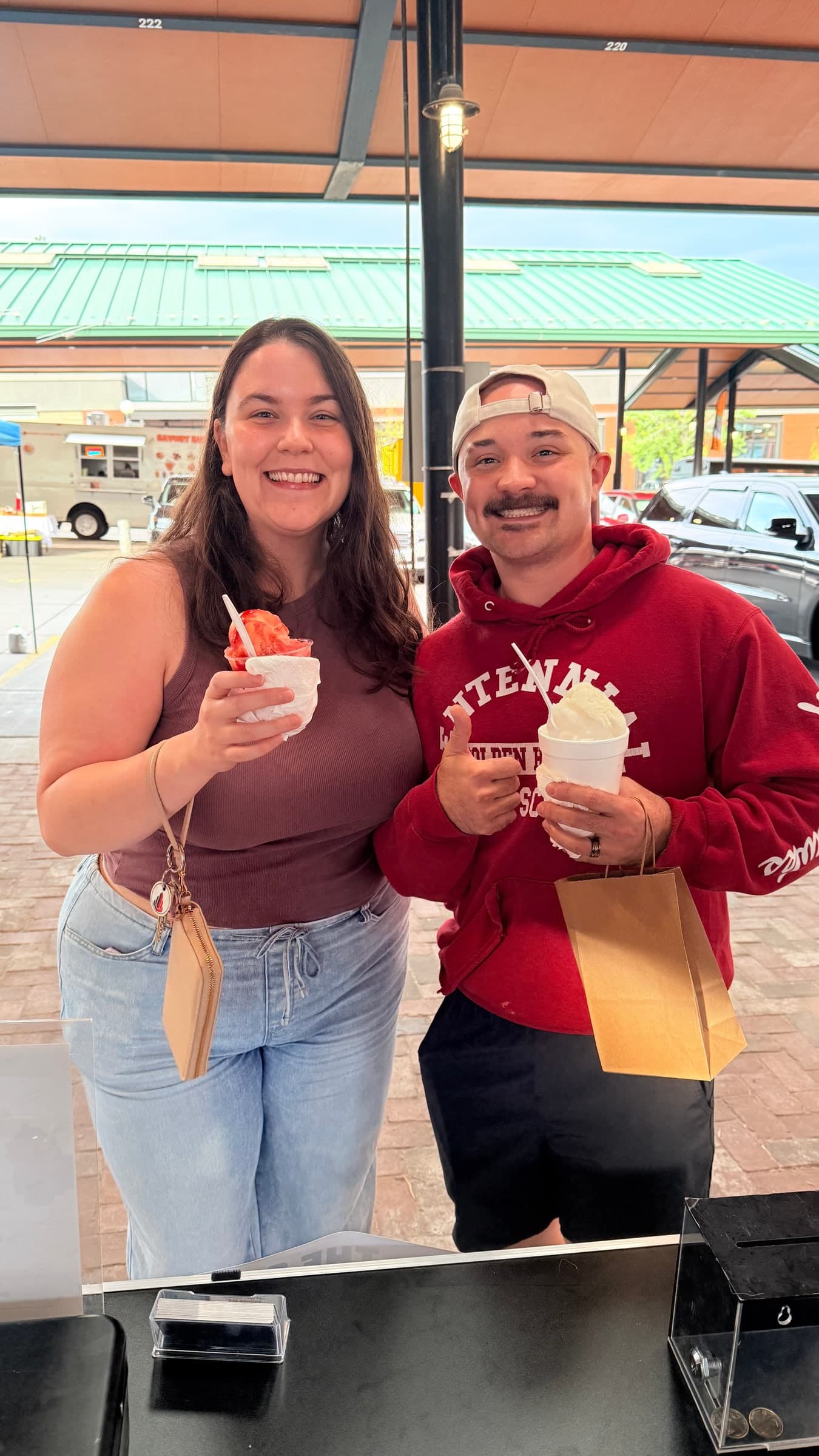 Two guests at the window holding sno balls, one giving a thumbs up
