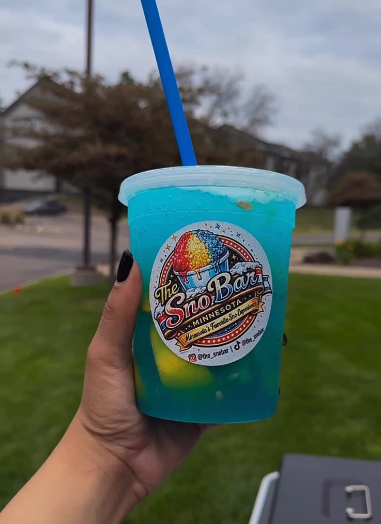 A Sno Bar cup of blue frozen lemonade held up outdoors