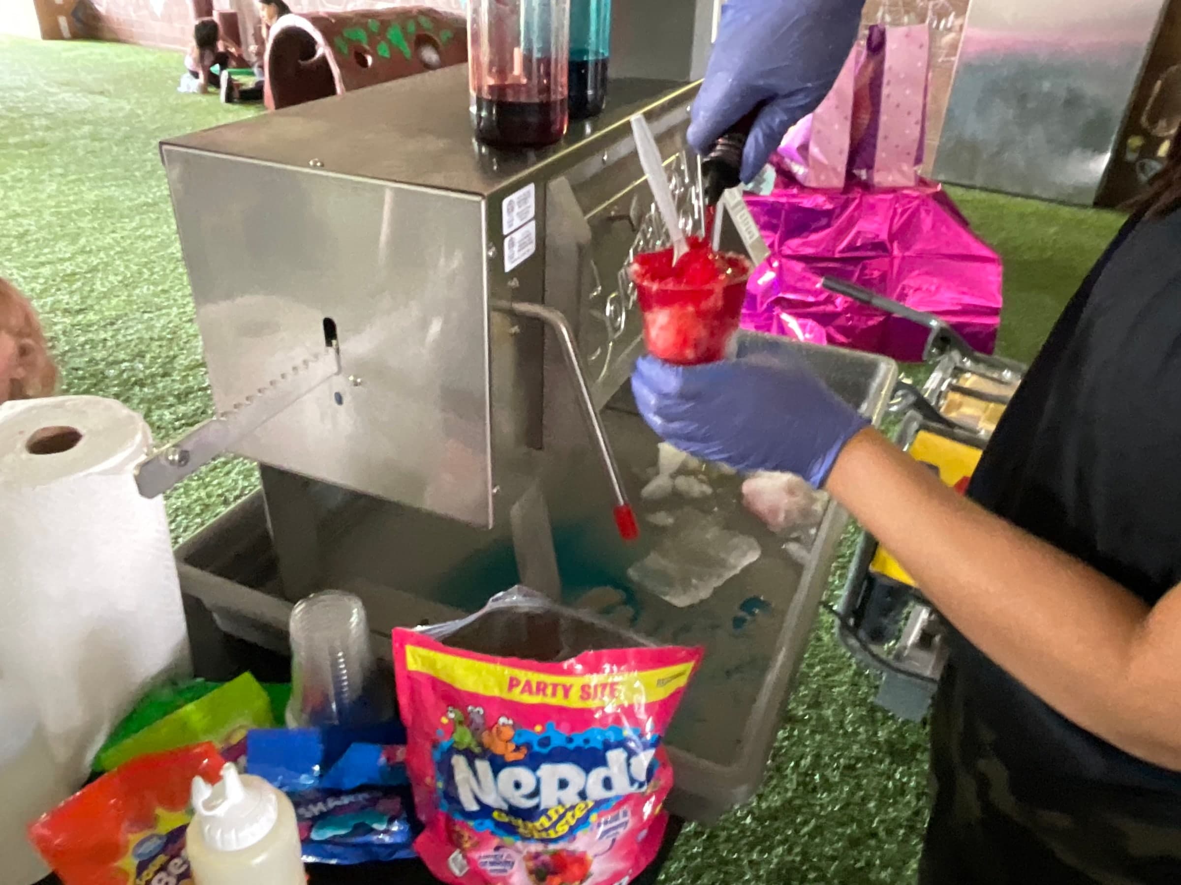 A gloved hand pouring syrup over a freshly shaved cup of ice
