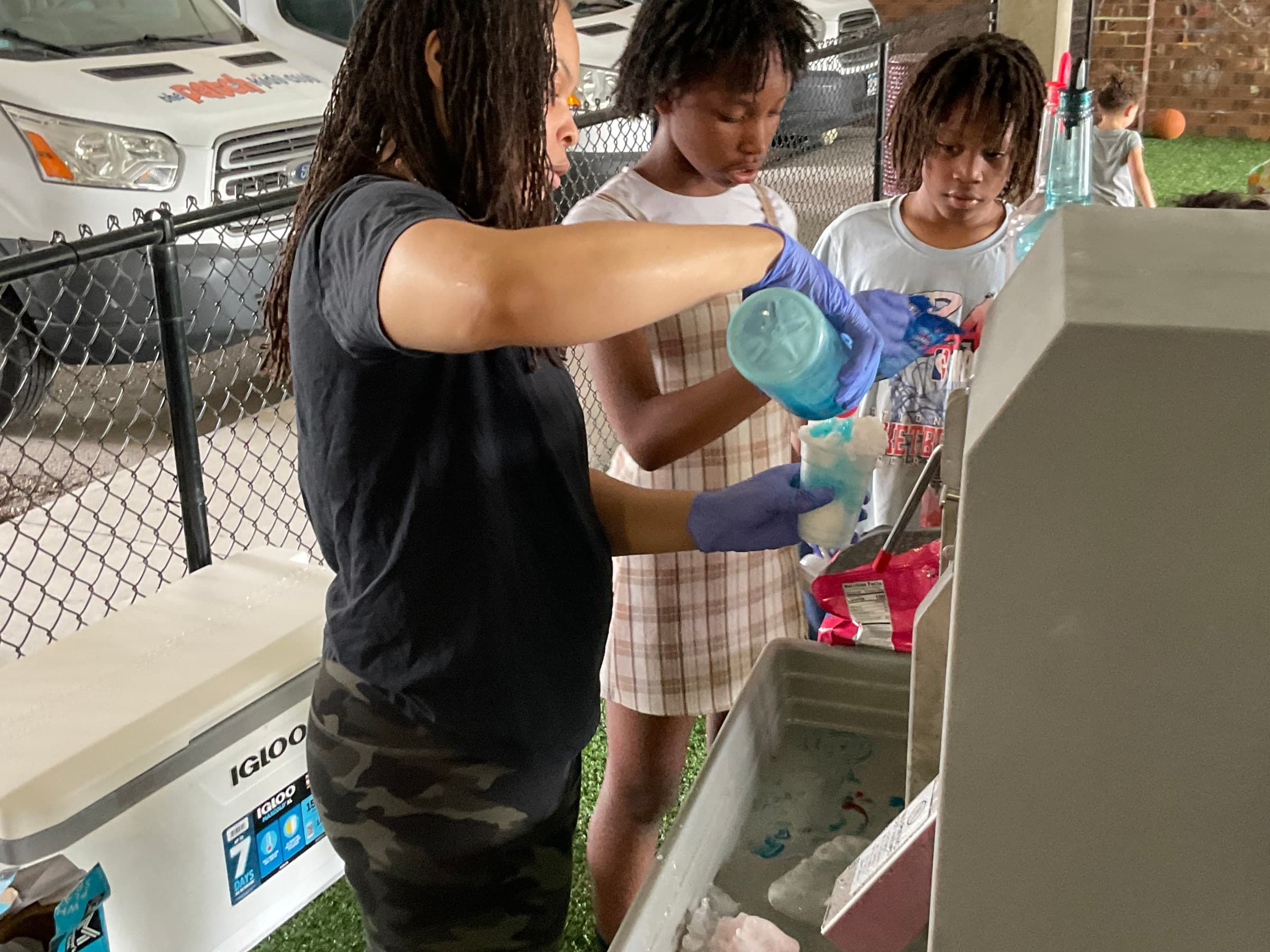 A Sno Bar server filling a cup at the shaved ice machine while guests wait